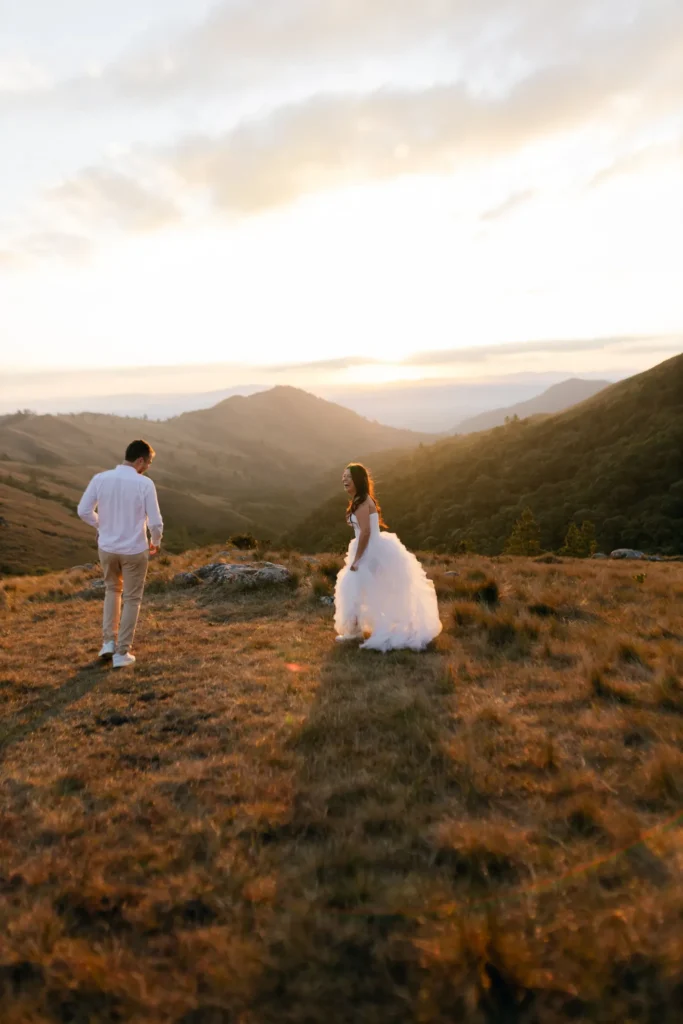 Couple en tenue de mariage marchant dans un paysage de montagne au coucher du soleil