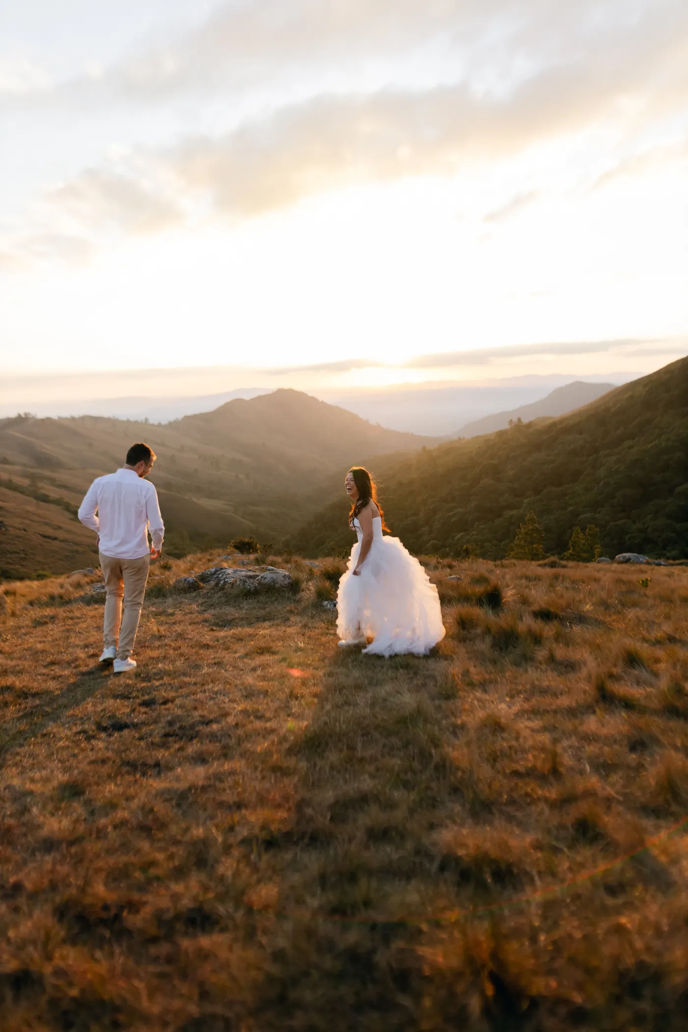 Couple en tenue de mariage marchant dans un paysage de montagne au coucher du soleil